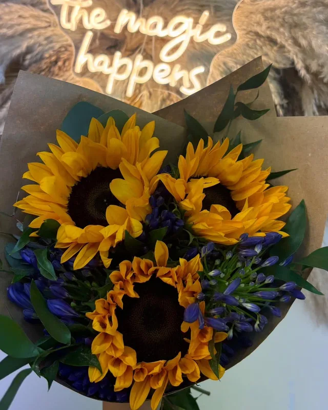 Sunflowers under the neon sign that reads this is where the magic happens