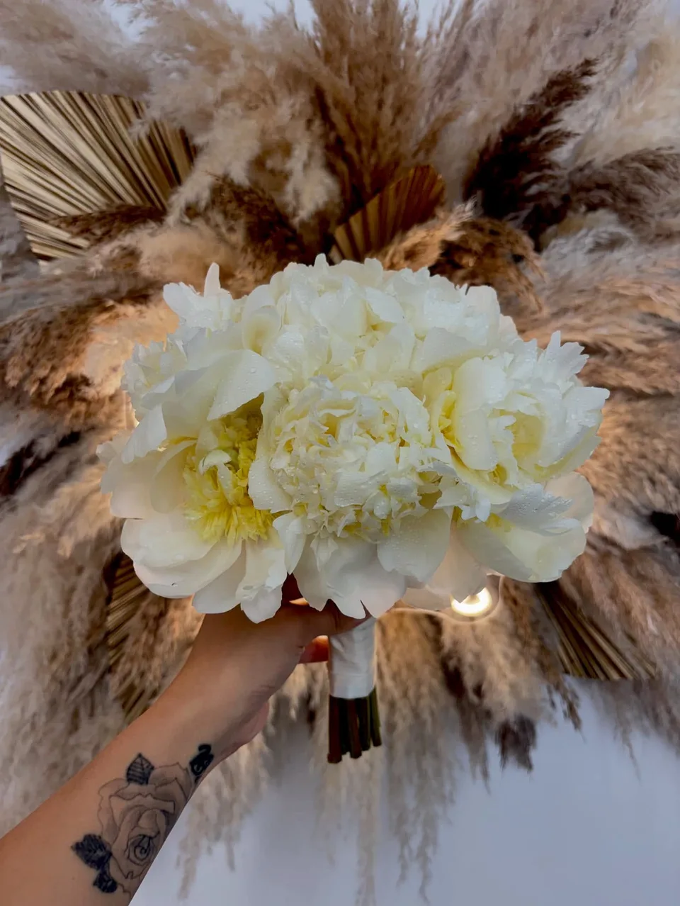 Ivory peony bridal bouquet framed by pampas grass